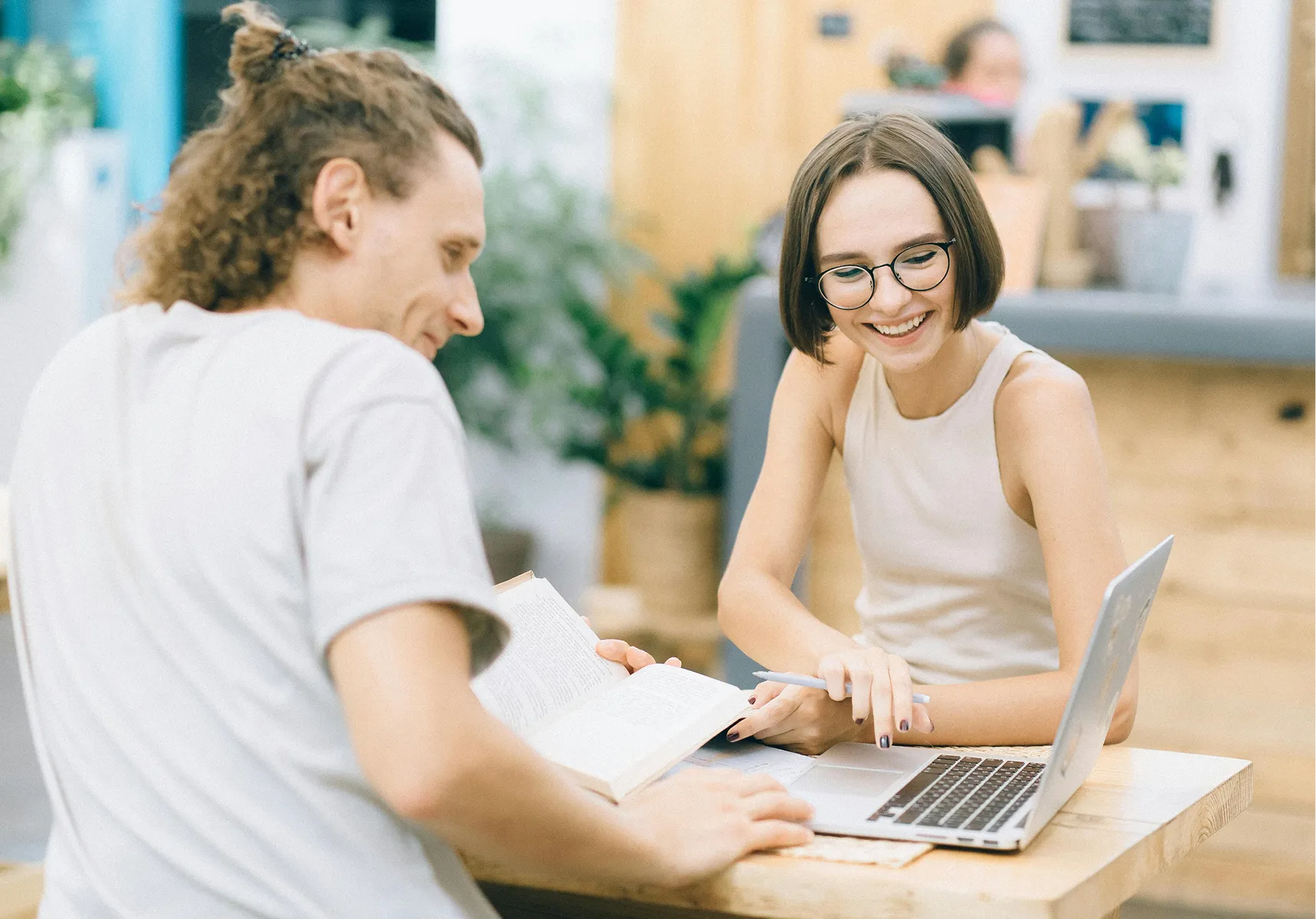 Two people smiling over a laptop in a bright cafe